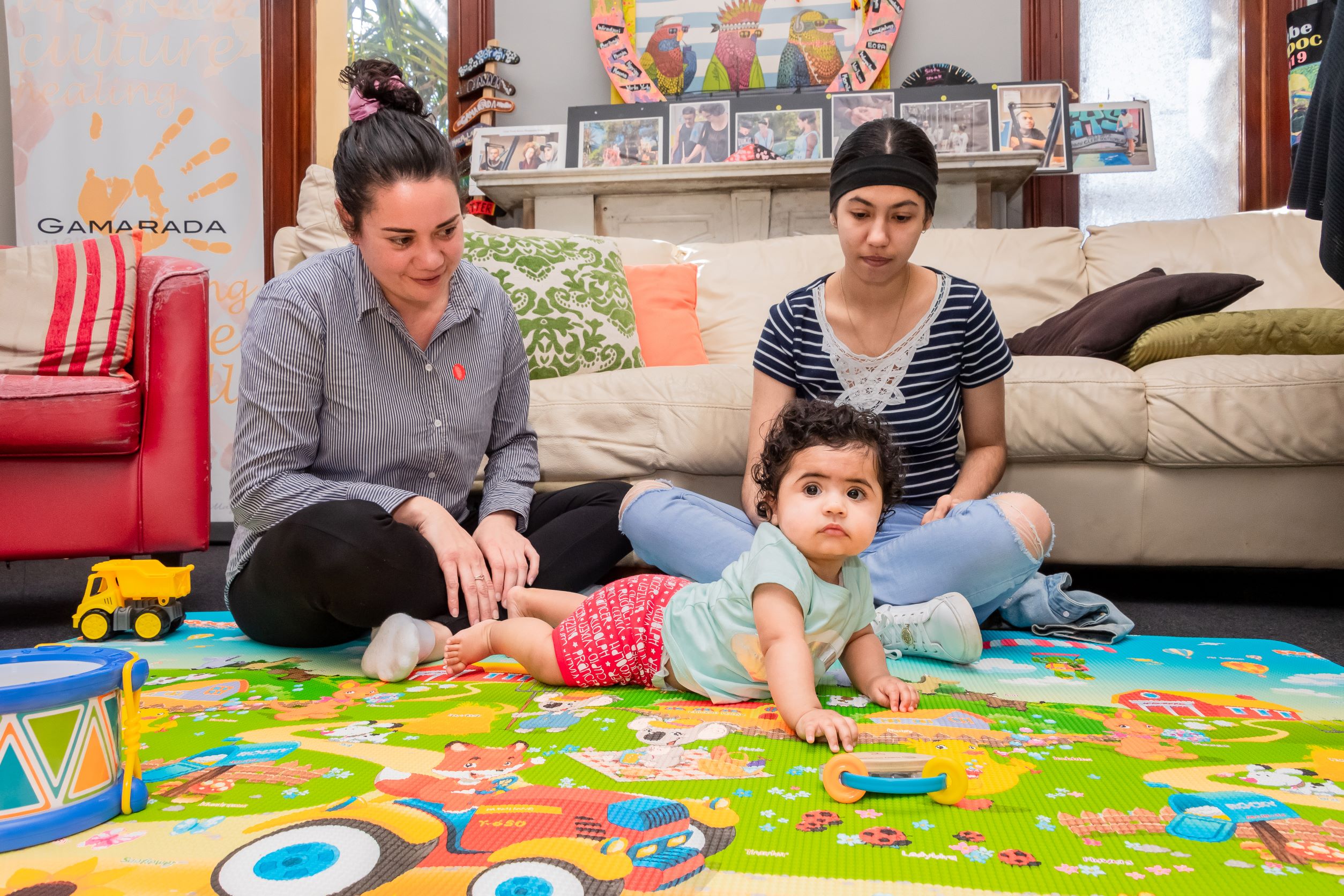 Two women sitting and  watching baby crawl on the floor