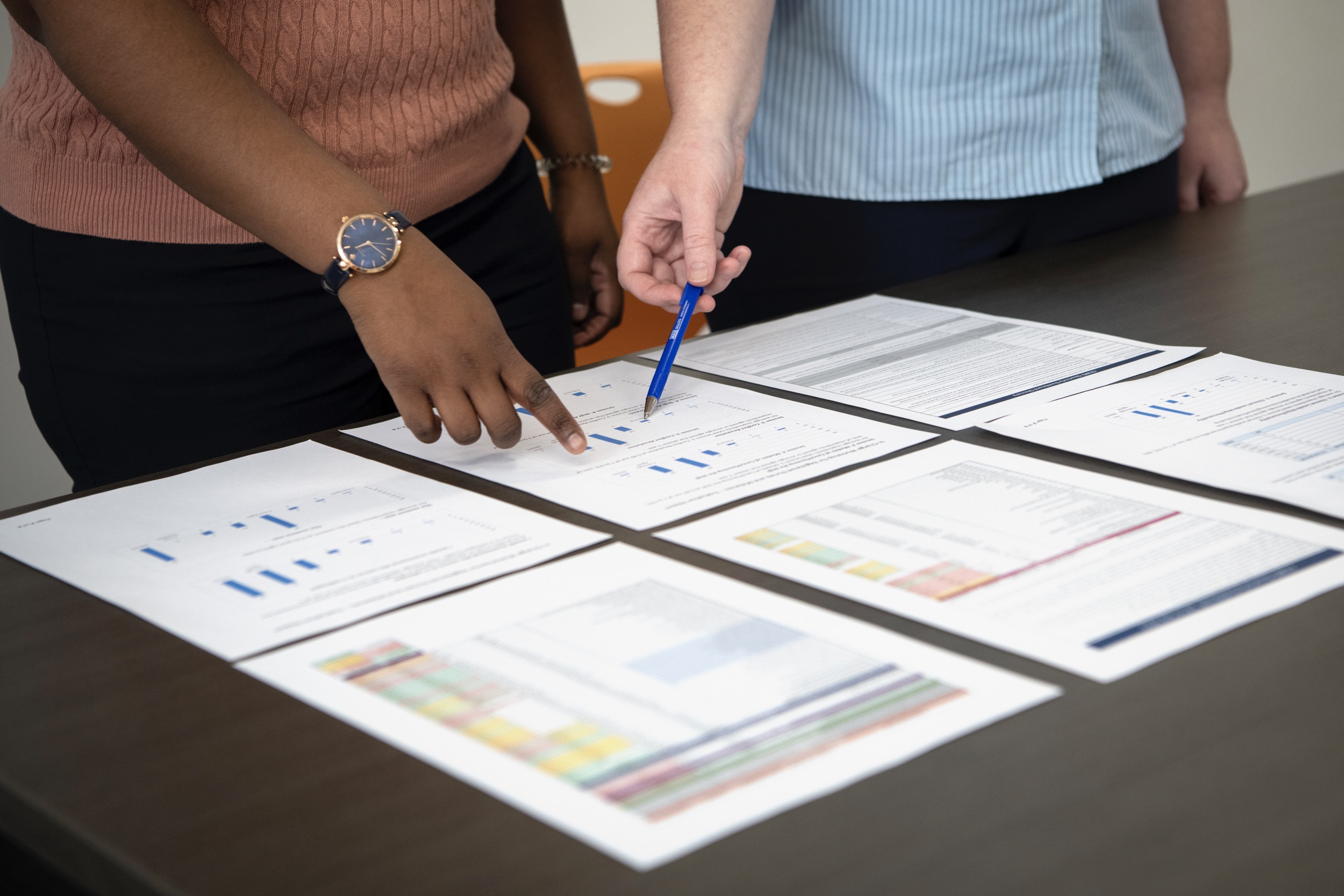 Two people reviewing reports laid out on a table.