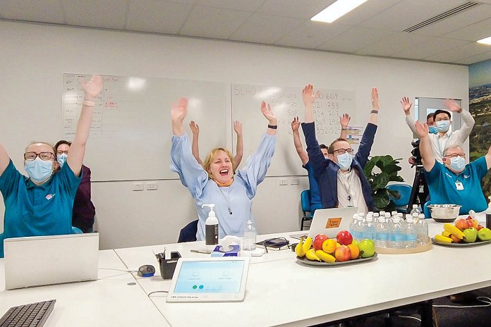 Group of people sitting around a large desk raising their hands in the air