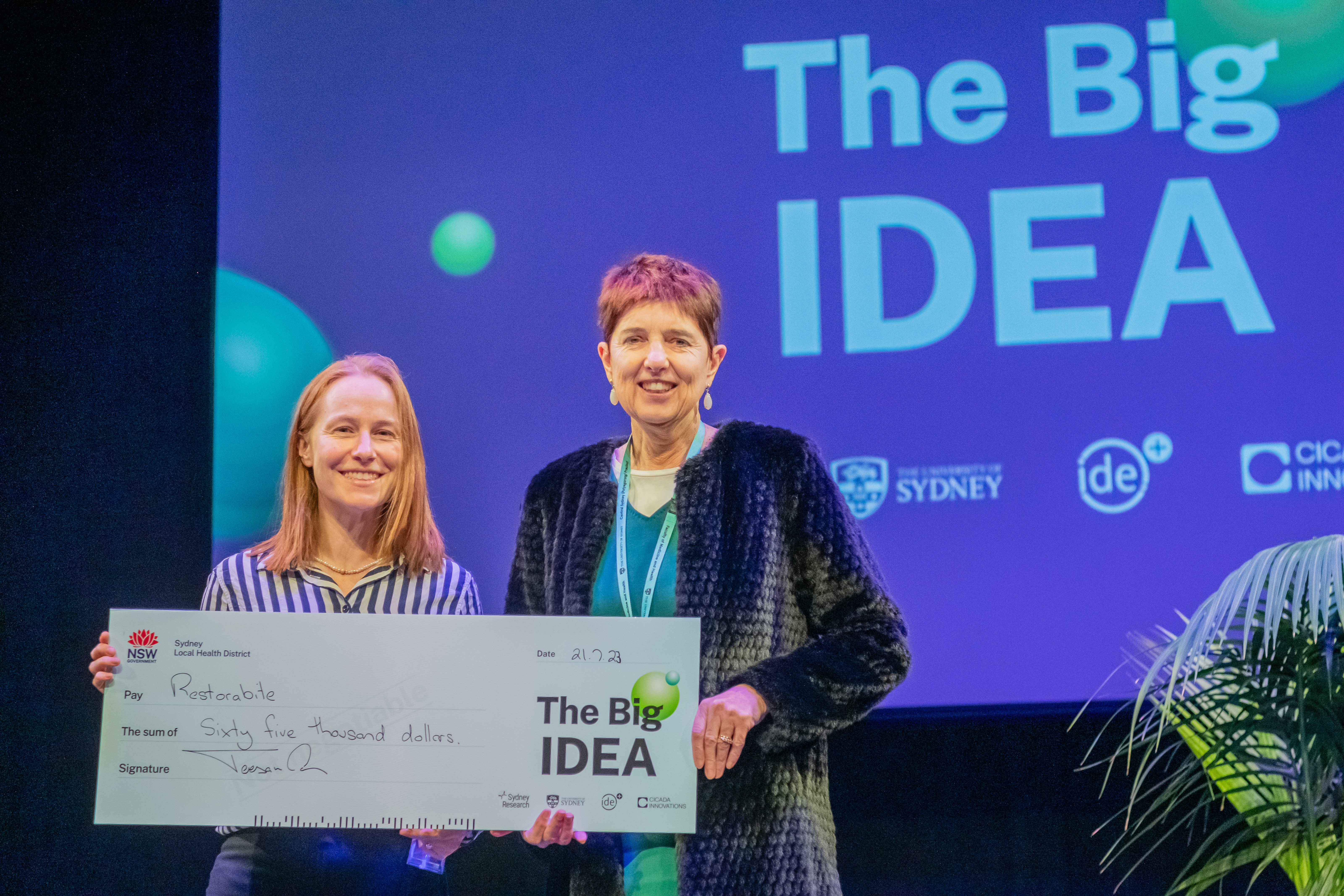 Two women pose while holding a novelty-sized cheque.