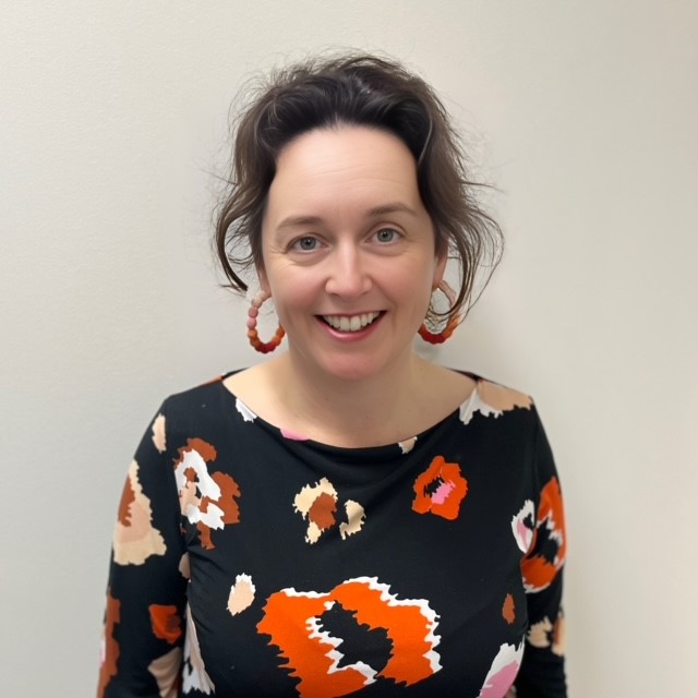 Professor Adrienne Gordon is smiling at the camera, wearing a black shirt with coloured pattern. 