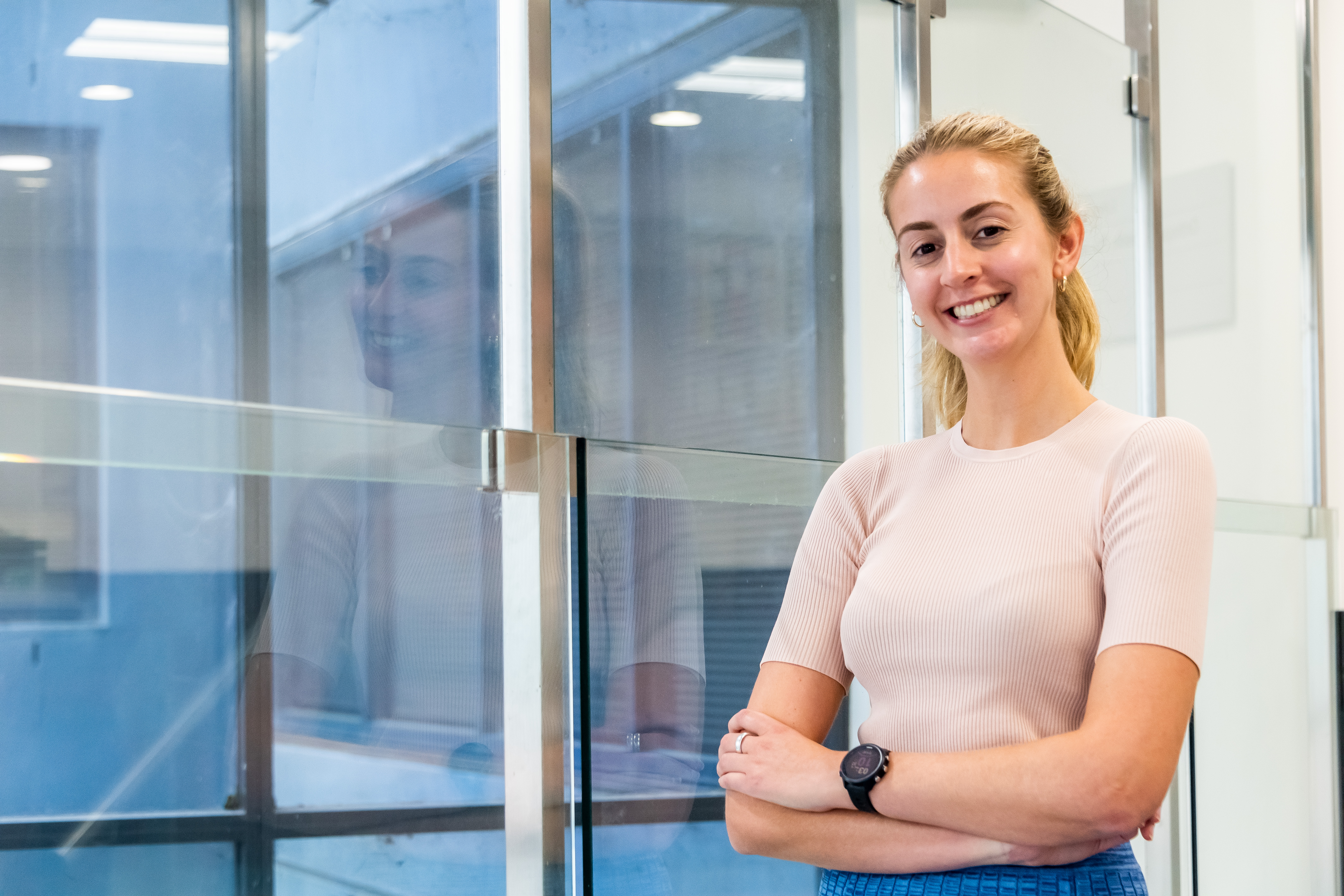 Speech Pathologist Stephanie Dunn is leaning against a window smiling towards the camera. 