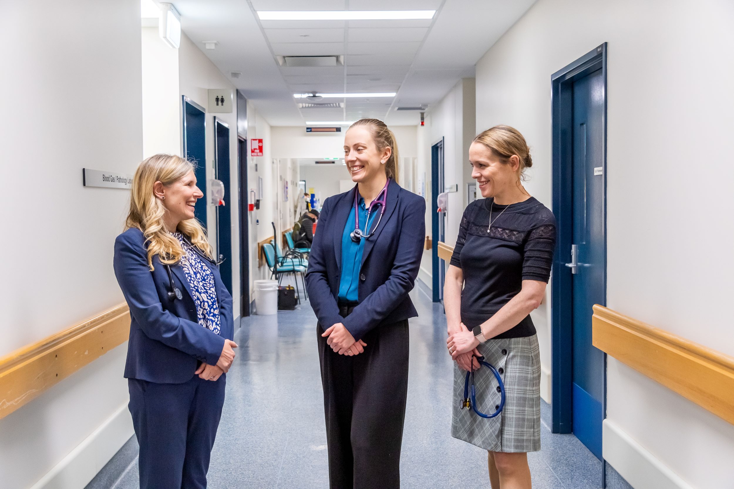 Three women standing together in a hallway talking 