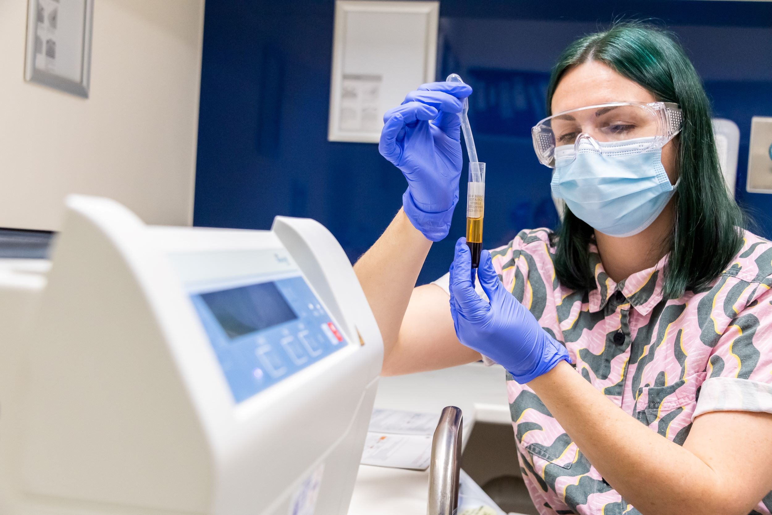 Woman wearing mask and goggles holding a pipette and test tube up to see contents