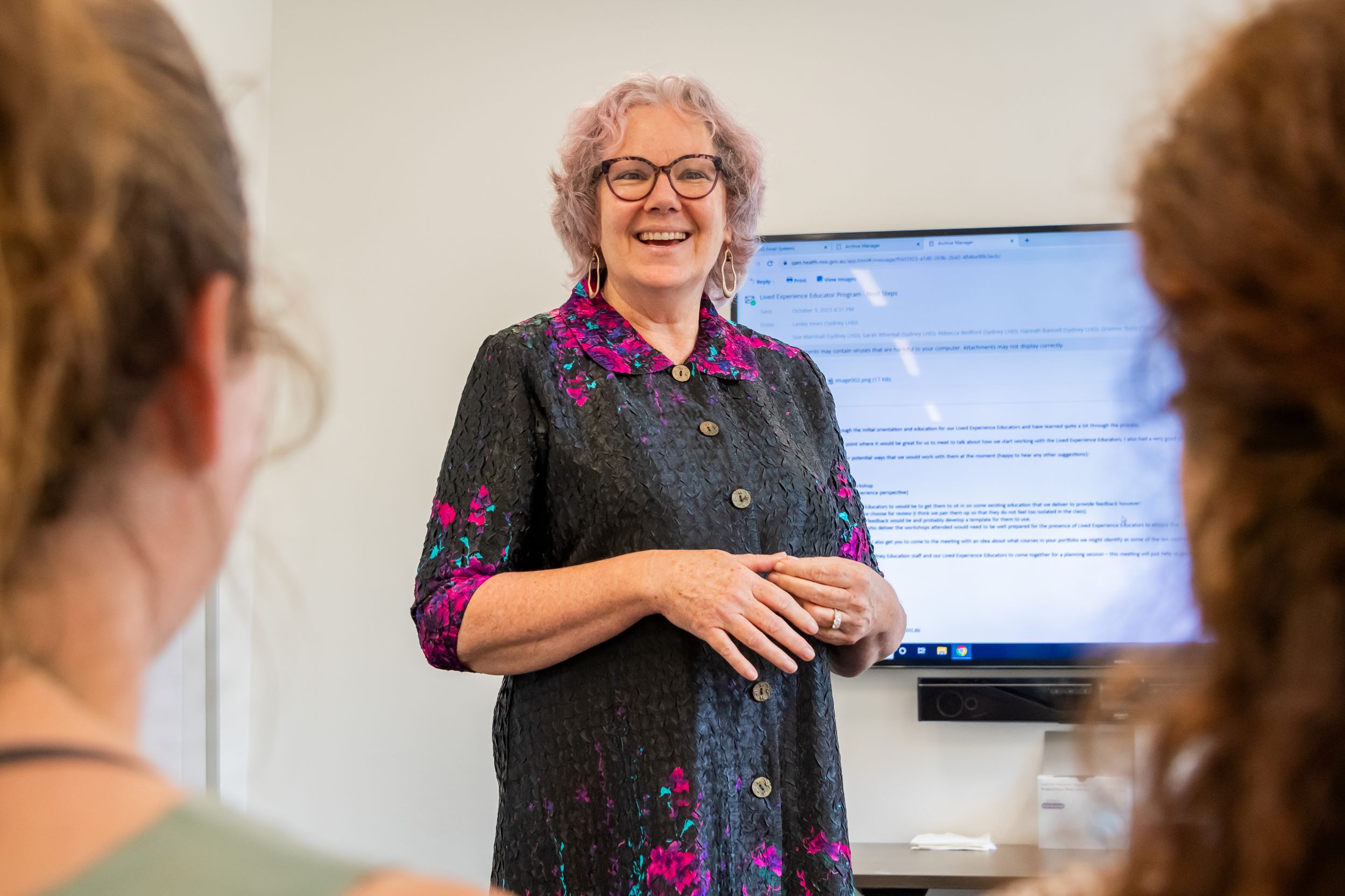 A woman stands at the front of a room in front of a crowd delivering an education session.