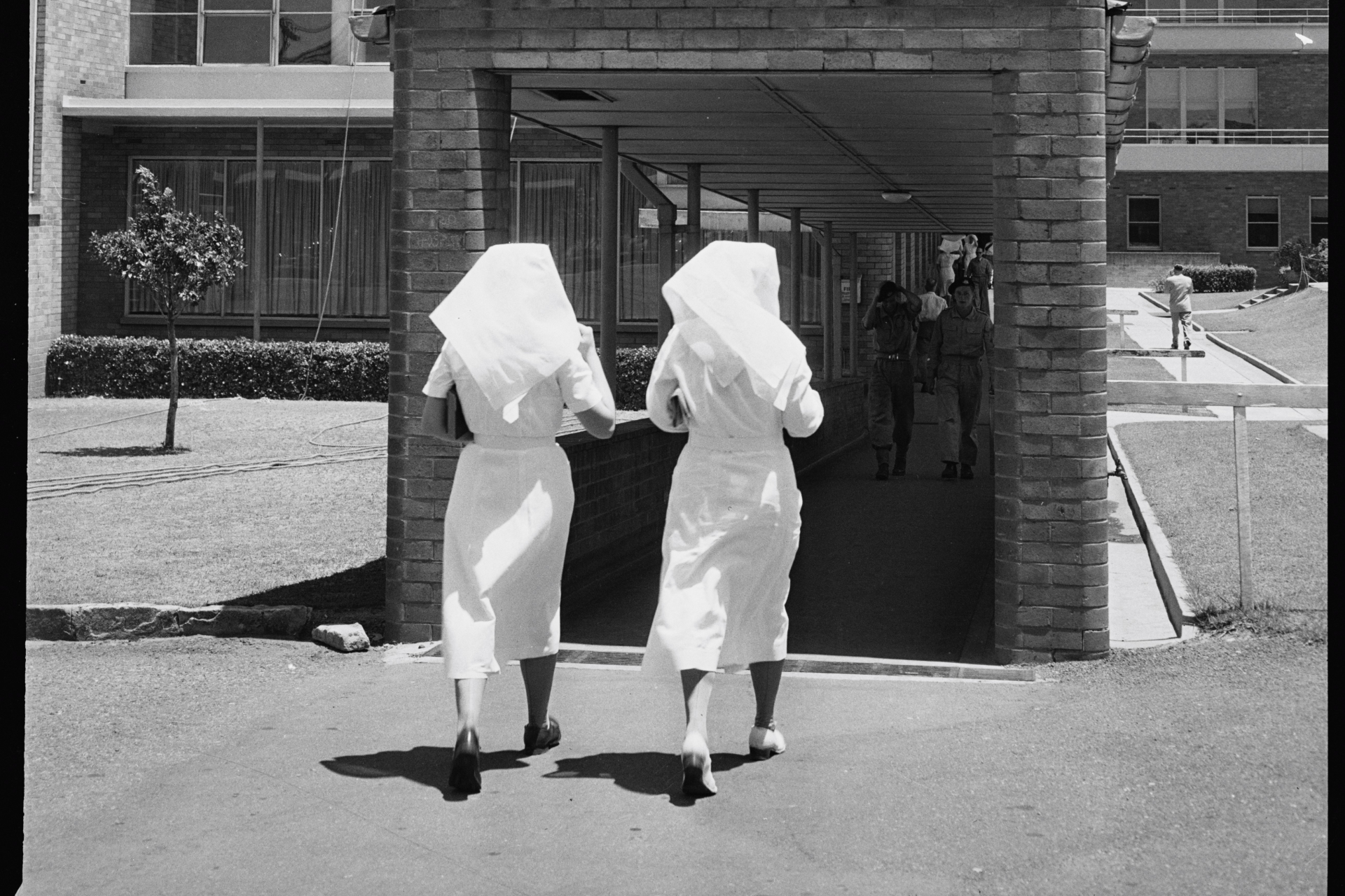 black and white photo of two nurses in uniform entering a building