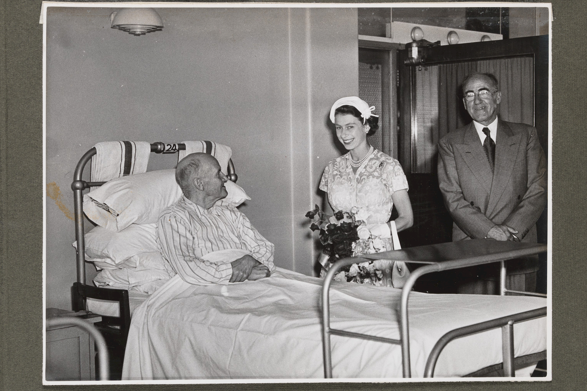 a black and white photo of a patient in a bed being visited by a woman and a man