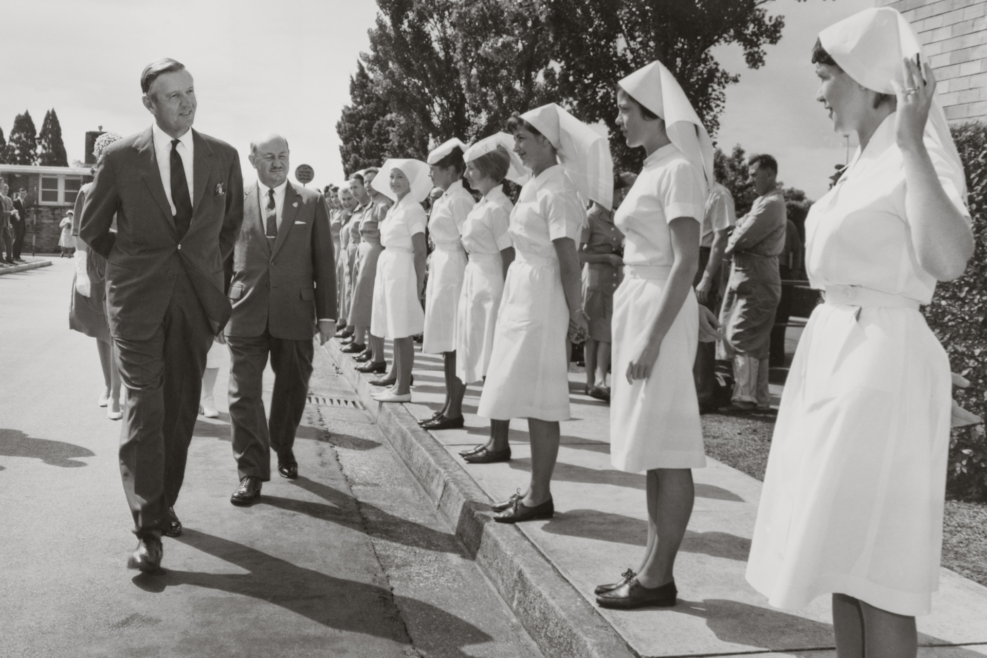 black and white photo of nurses in uniform lining streets with man walking past