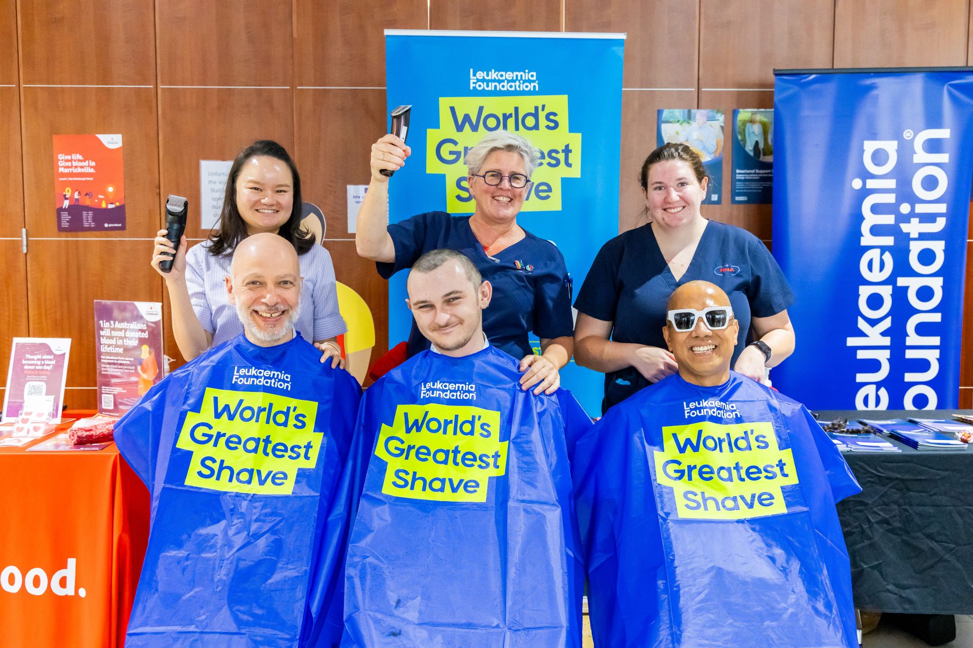 people with capes draped preparing to have their head shaved