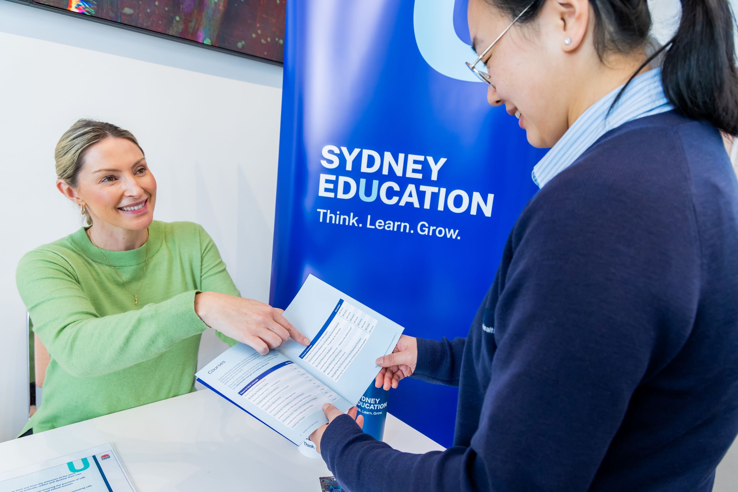 Woman sitting down at a desk handing a piece of paper to someone standing on the other side