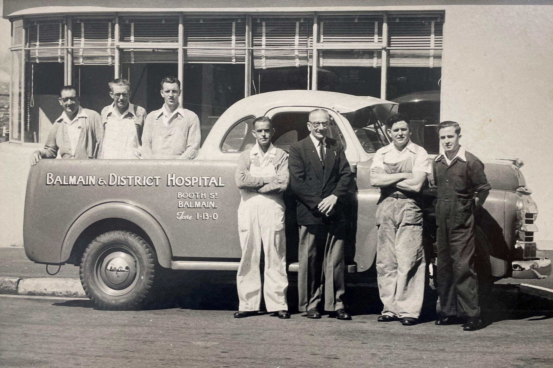 Black and white photo of men standing outside and behind a hospital car 1953