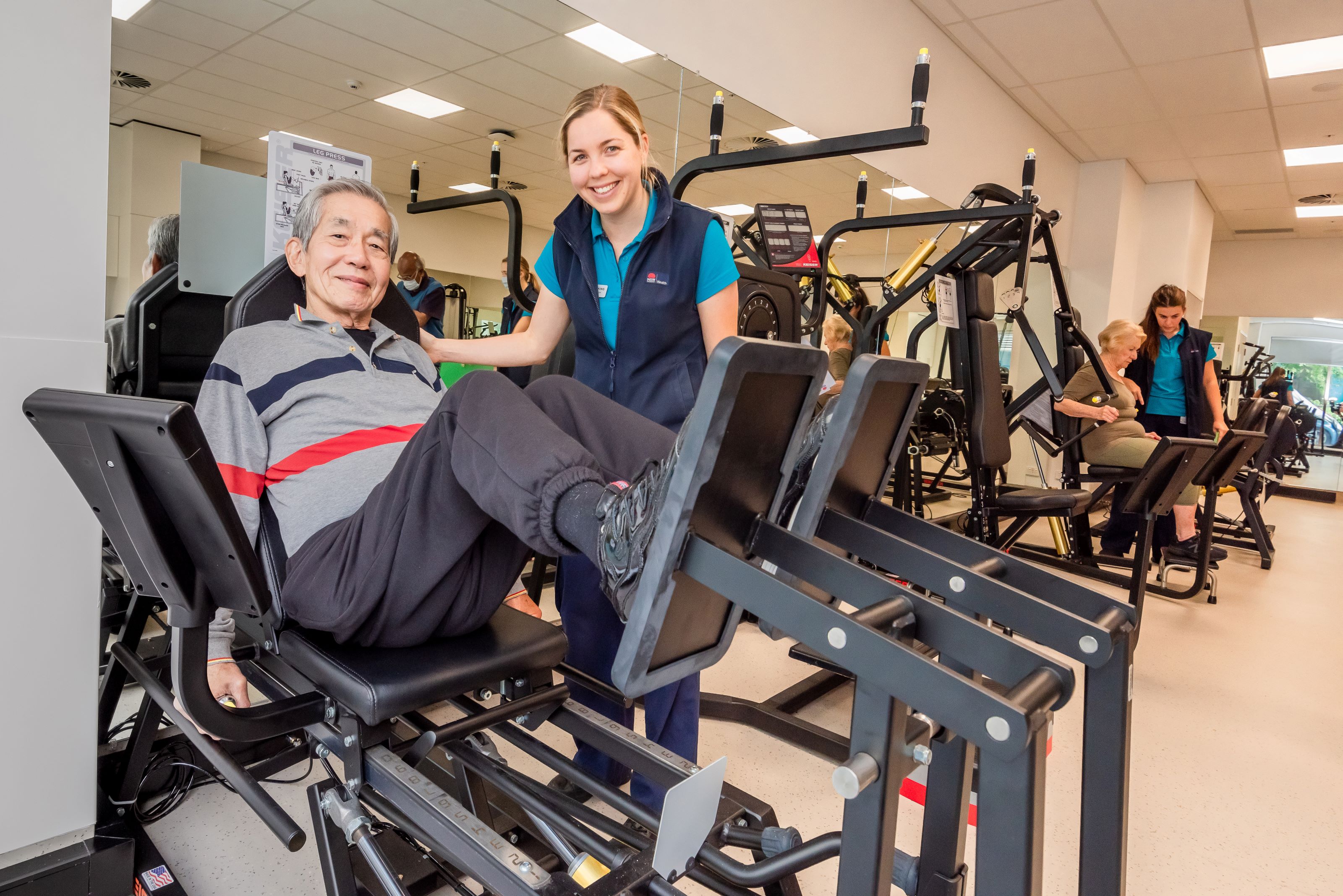 A clinician stands next to a man using exercise equipment 