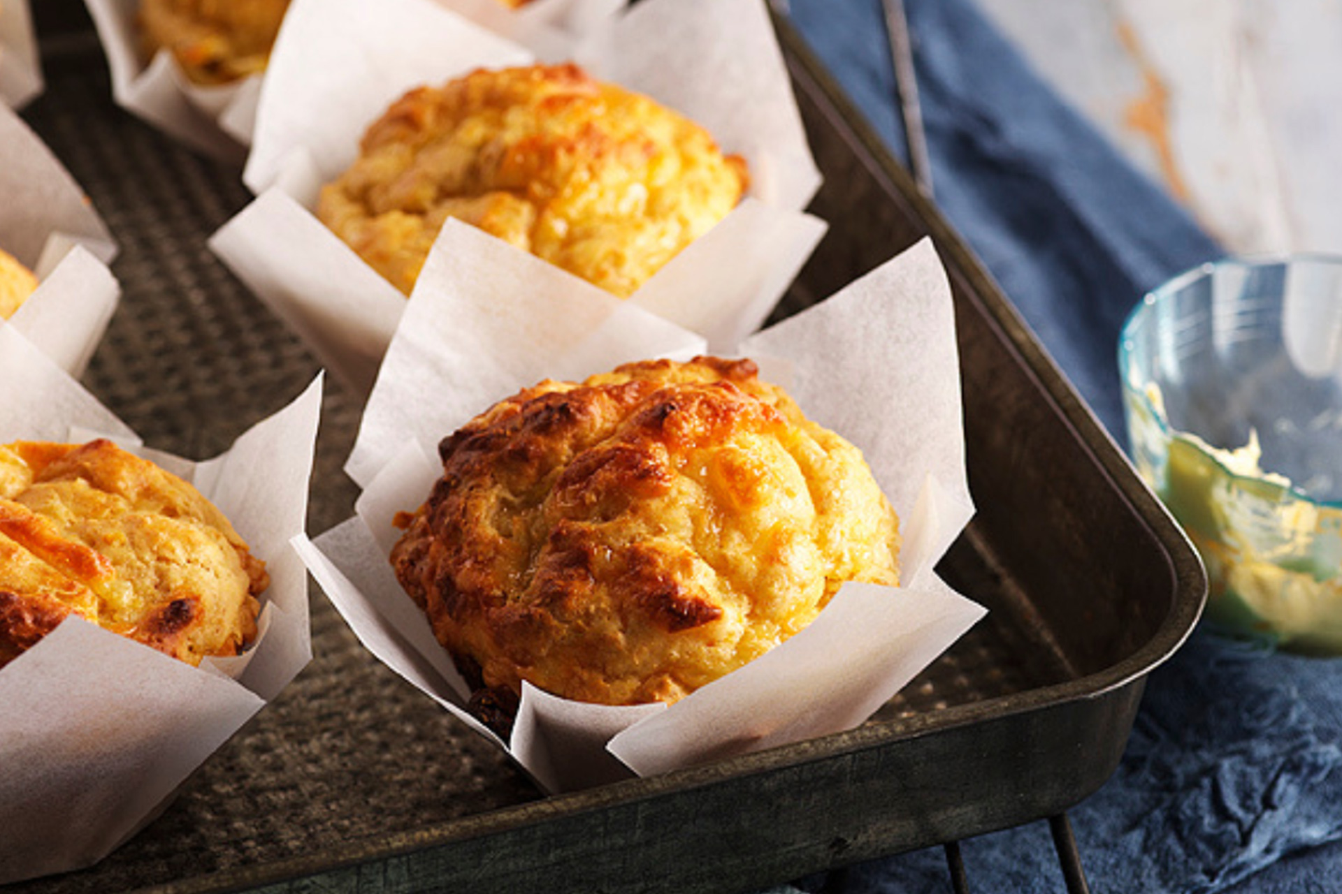 Cheesy corn mufins sitting in baking tray on navy blue cloth