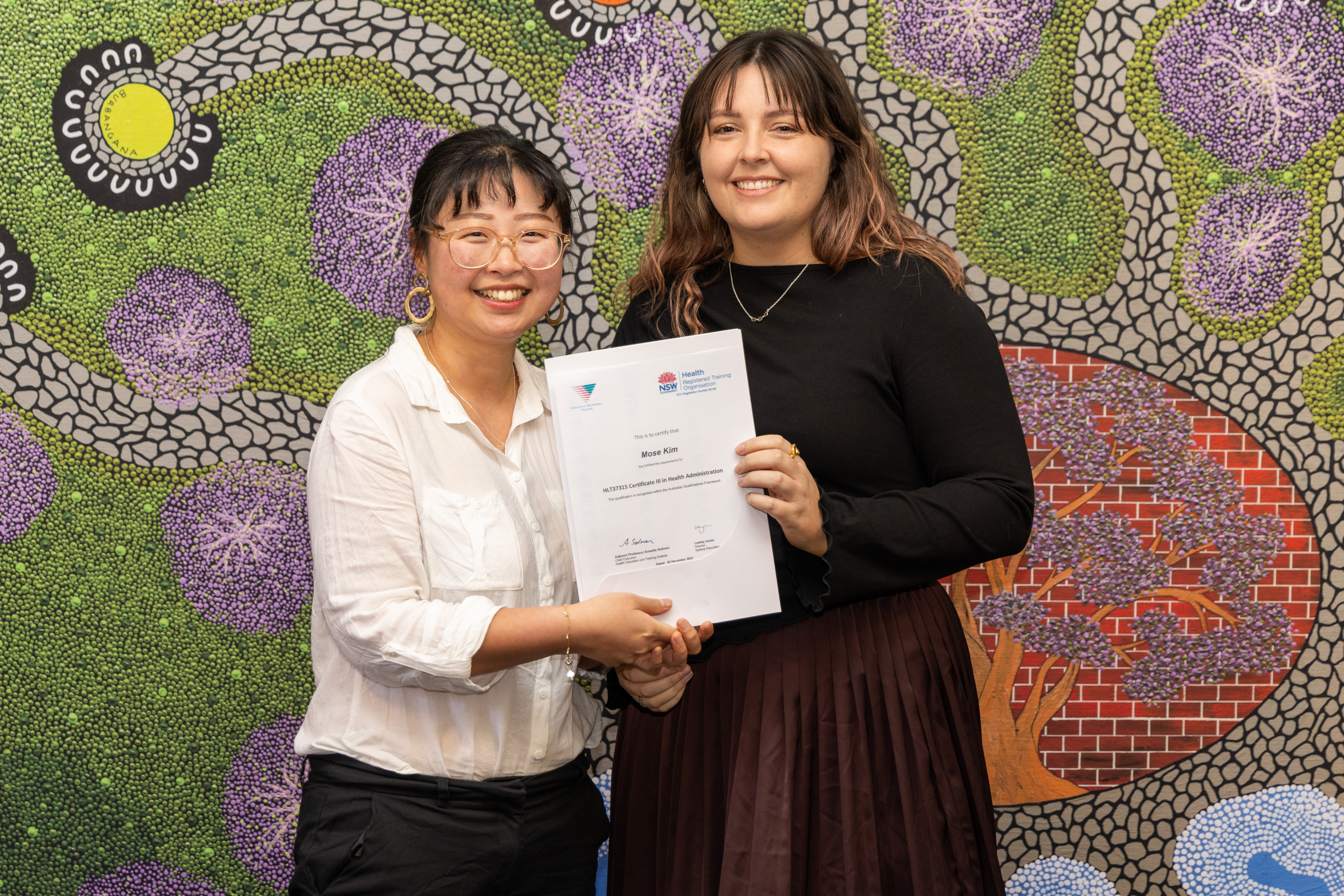 Two women stand smiling at the camera holding a certificate