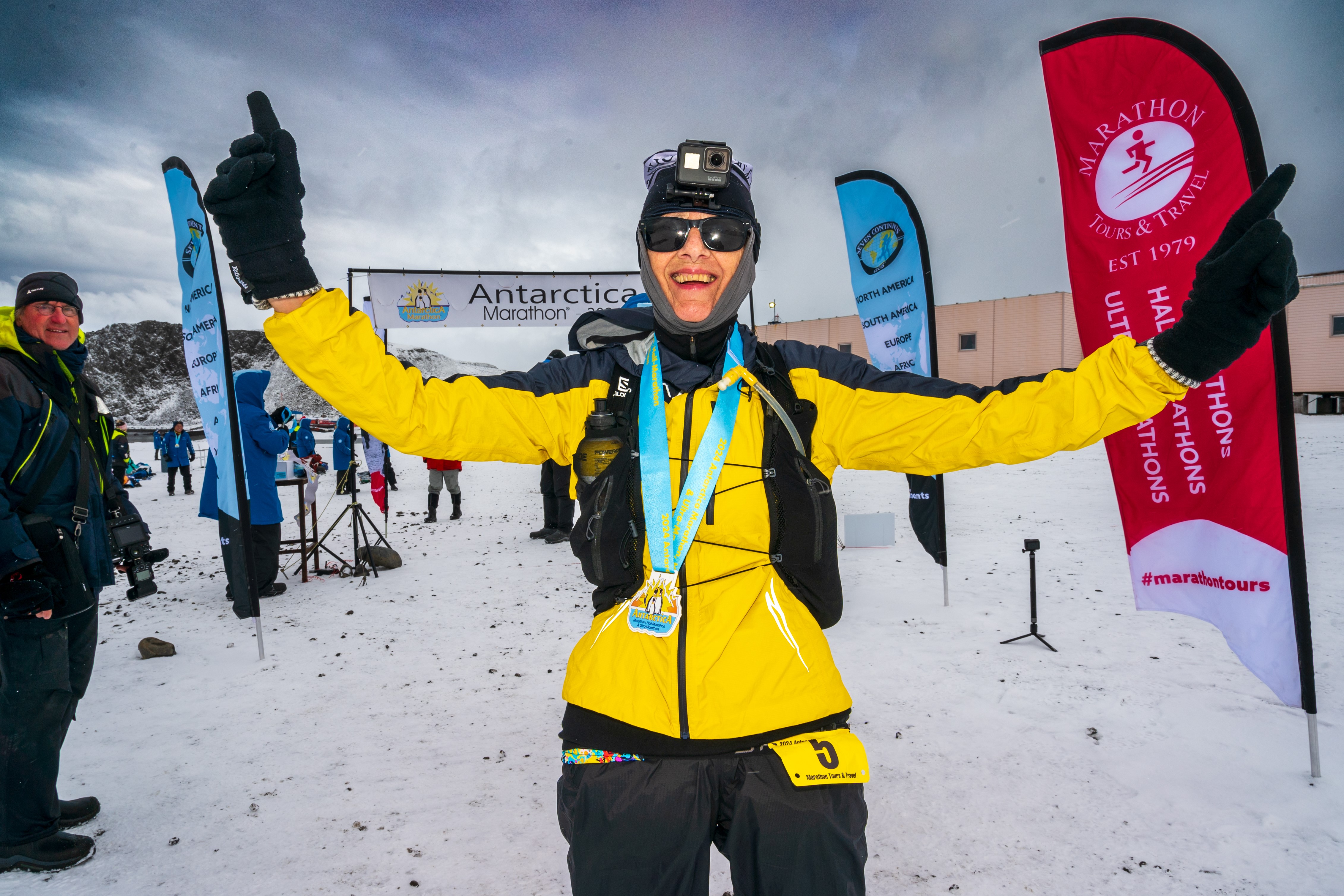 A woman stands on the snow with arms up and smiles