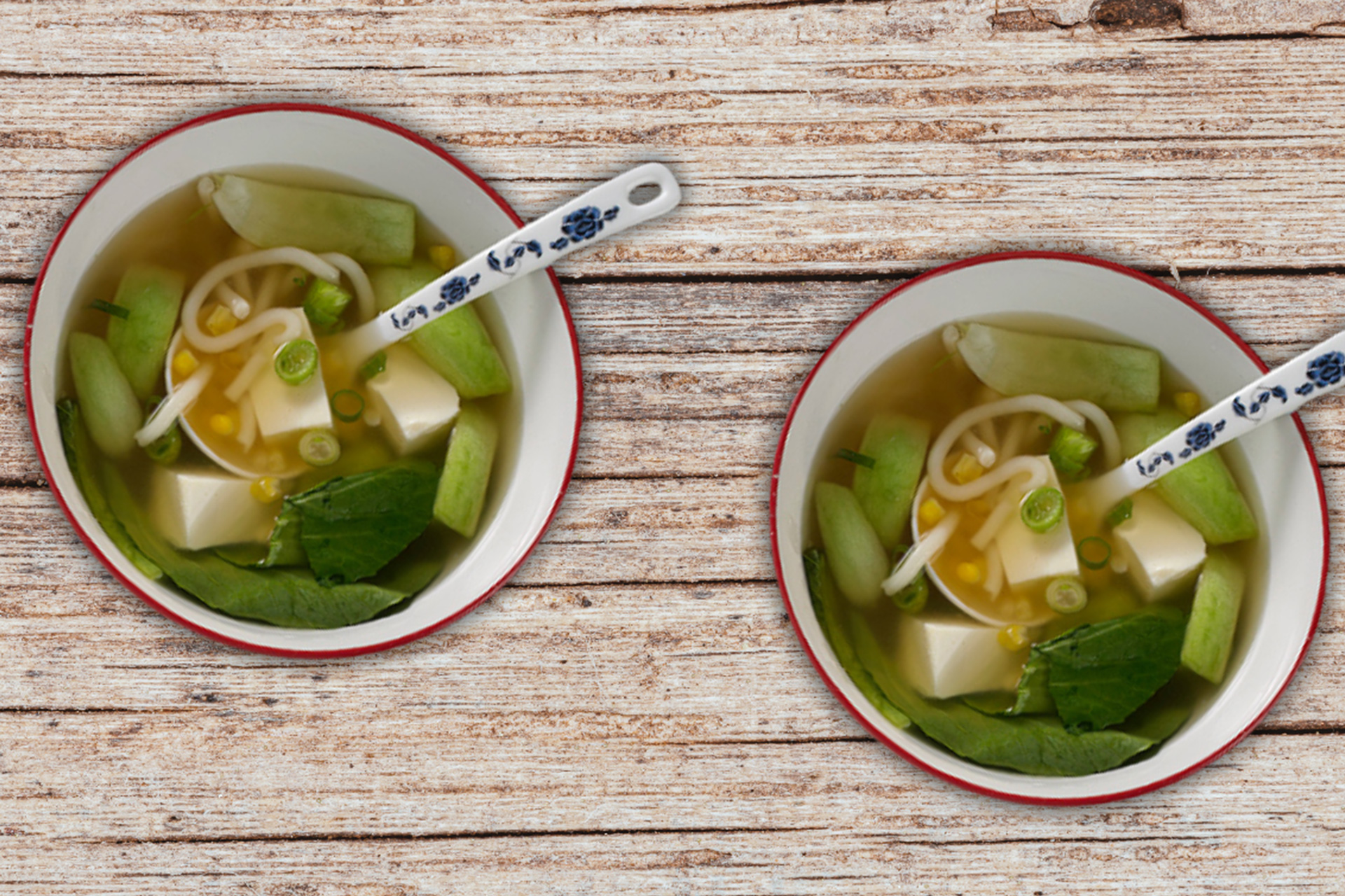 Two bowls of noodle soup with asian greens served in bowls on wooden table