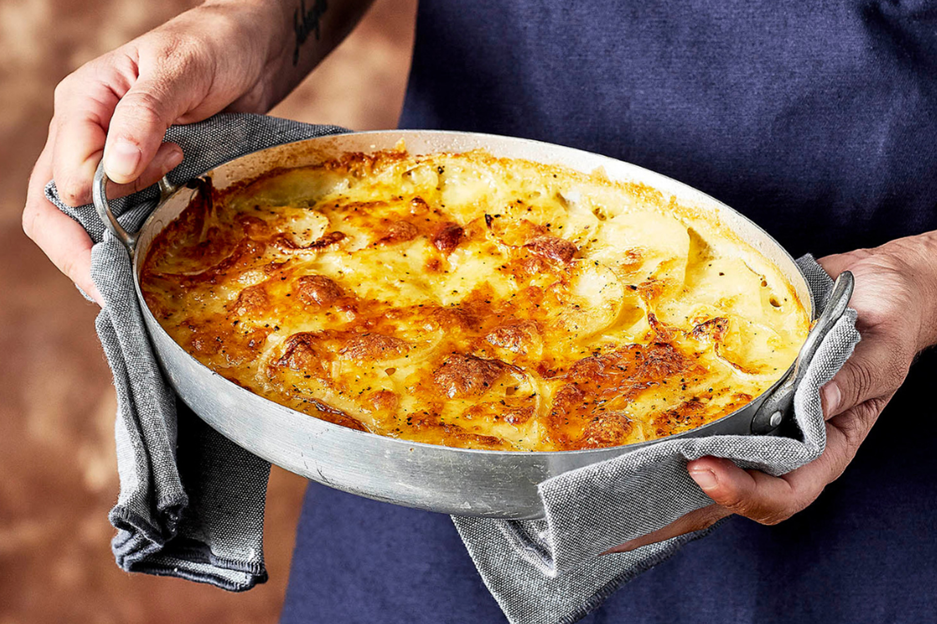 Man holding potato bake in silver baking dish with grey heat mitts