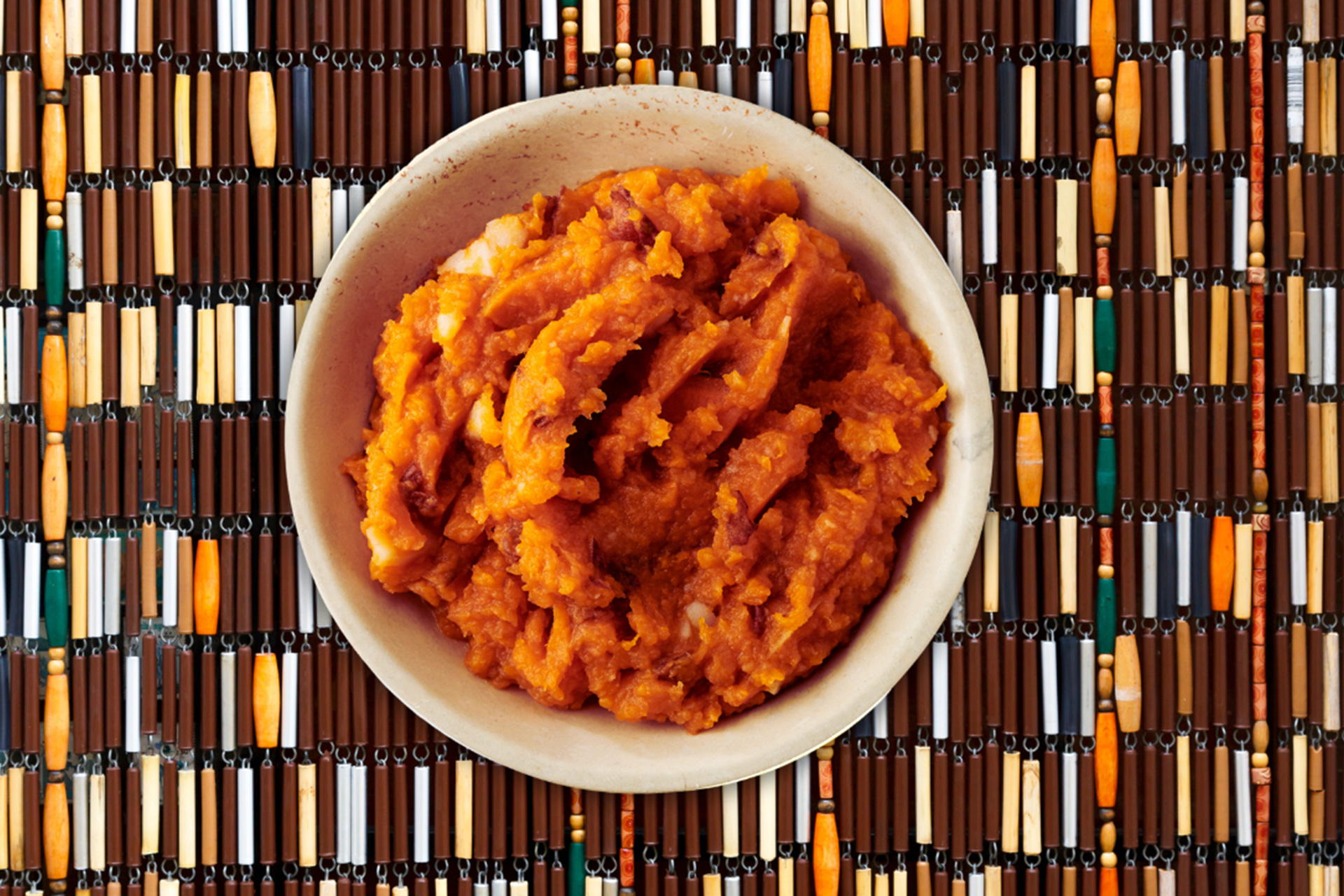 Sweet potato smash served in cream bowl on brown beaded placemat