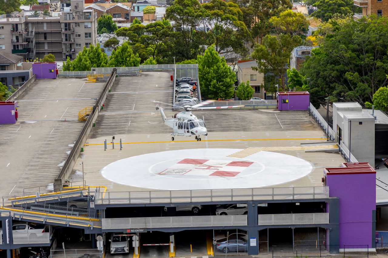 A helicopter hovers above a helipad on the rooftop of a car park.