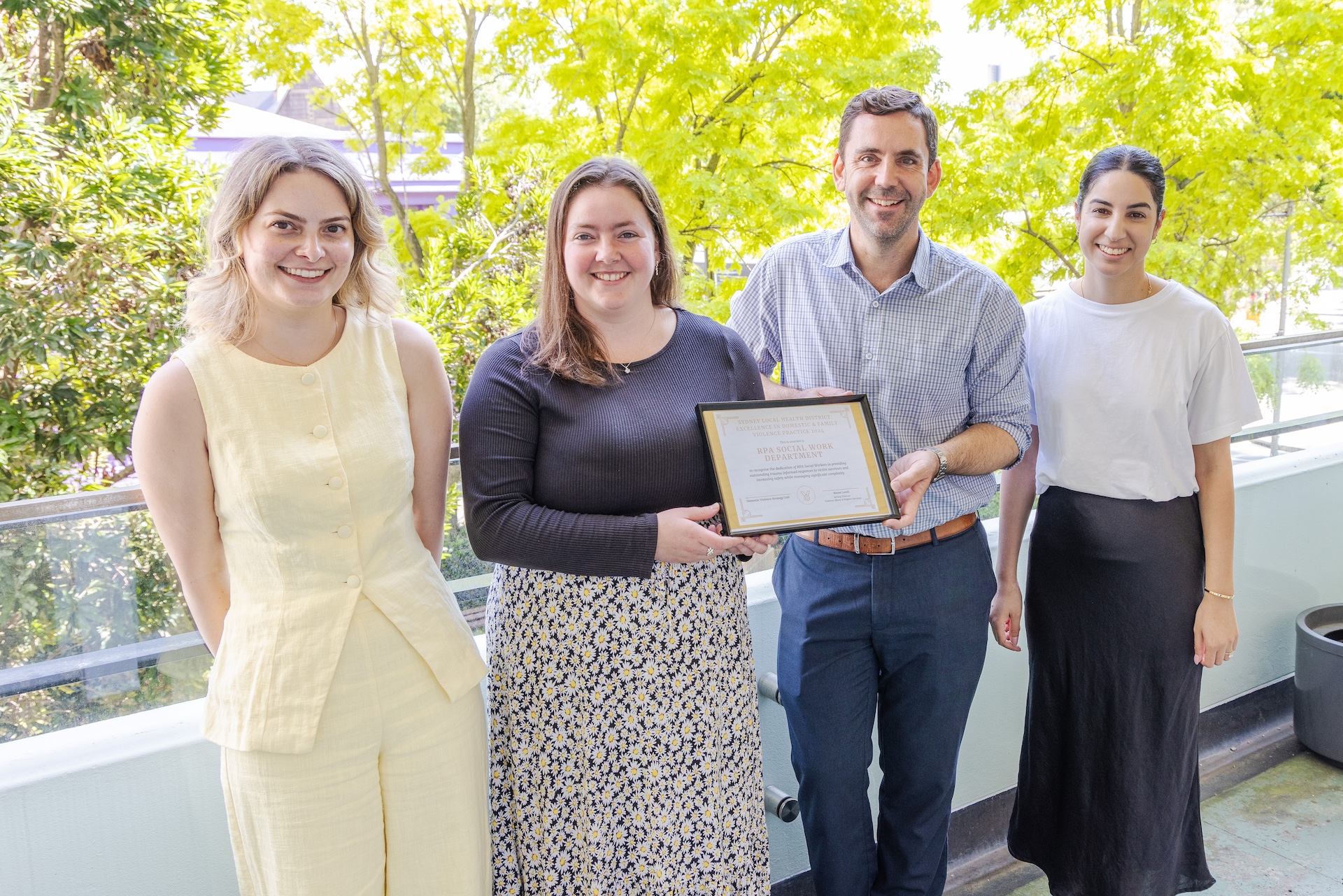 group photo of 4 members of the RPA social work department standing at a balcony, holding their award certificate