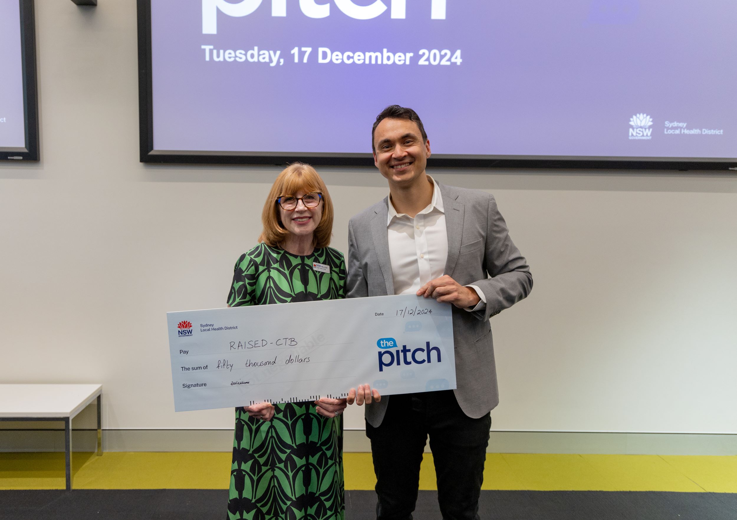 Two people standing next to each other holding a giant cheque