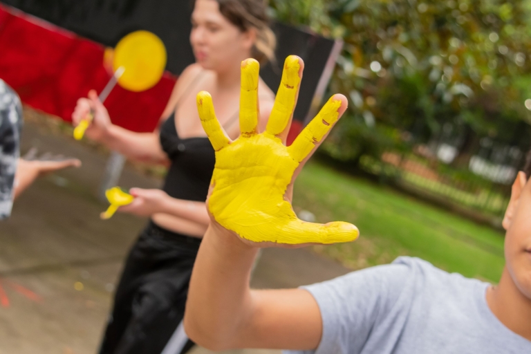 Child holding up painted hand; with Aboriginal flag in background