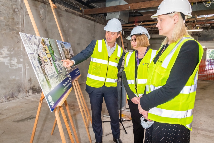 Executives in personal protective equipment look over redevelopment designs in a semi-constructed room.