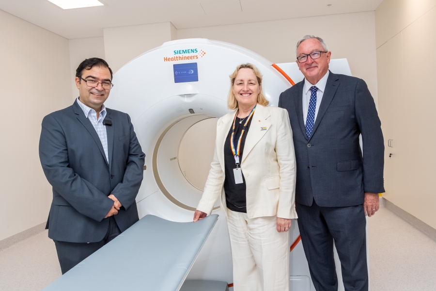Three people standing in front of a medical scanning machine