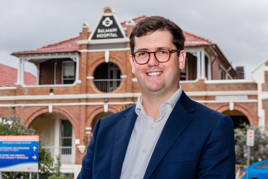 Smiling man stands in front of red brick hospital building.