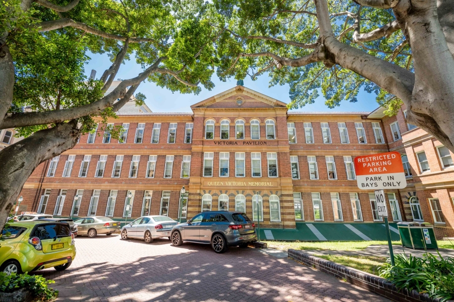 A red-brick Victorian building framed by trees with cars parked in front.