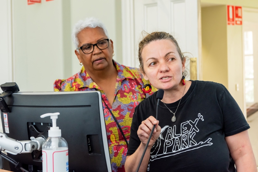 Two women stand at a lecturn as one of them holds a microphone to pitch their funding proposal.