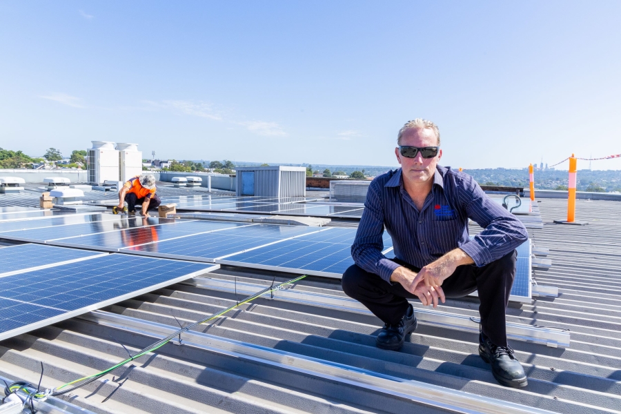 Man squatting on the roof of a building with solar panels behind