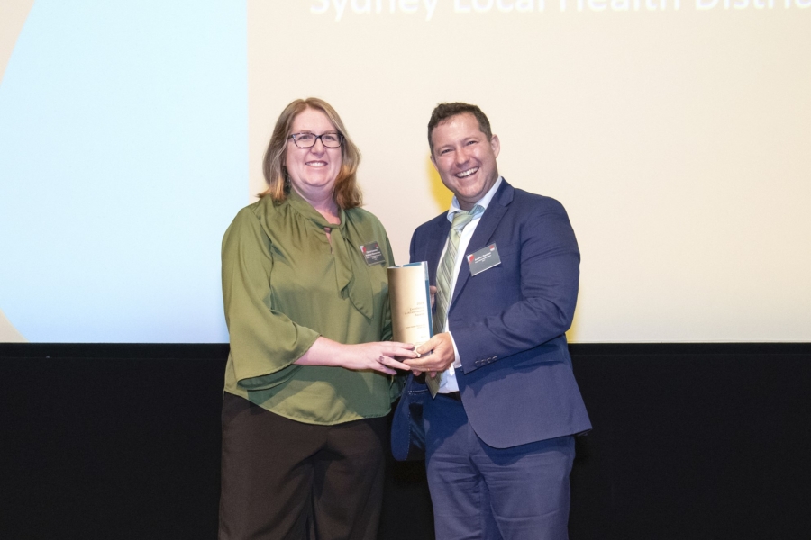 Woman and man standing on stage; woman receiving award from