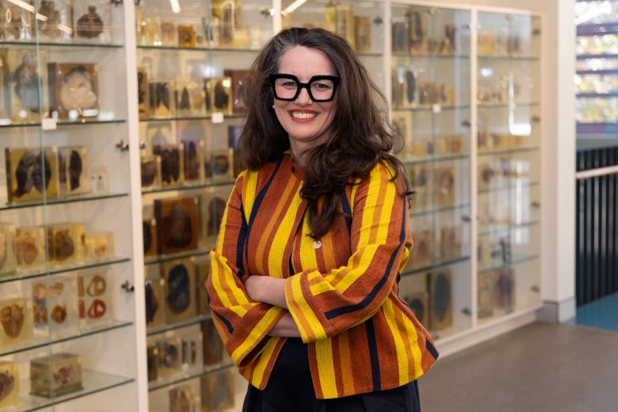 A woman stands and looks at camera smiling.