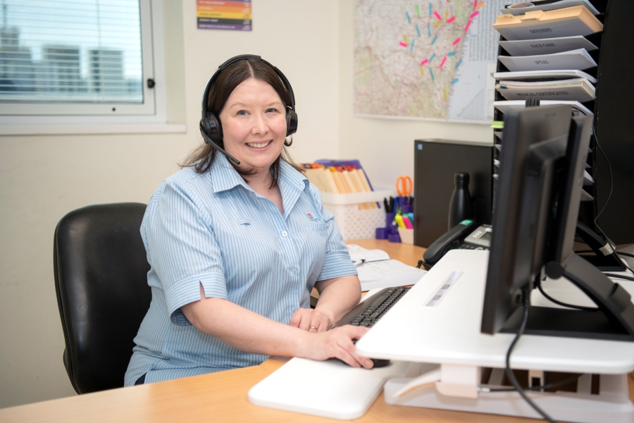 A woman sits at a desk with a headset on smiling at camera