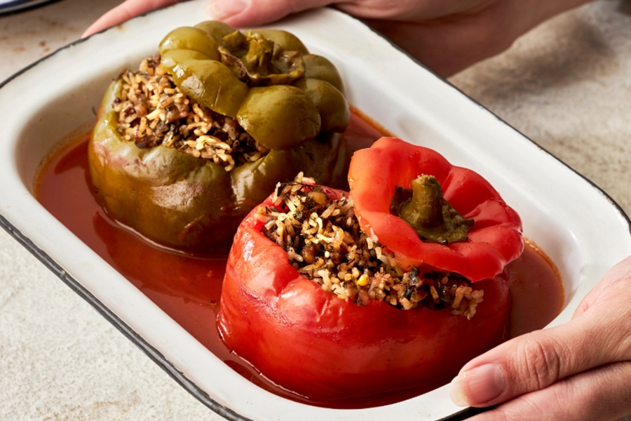 Hands holding baking tray with stuffed roasted capsicum