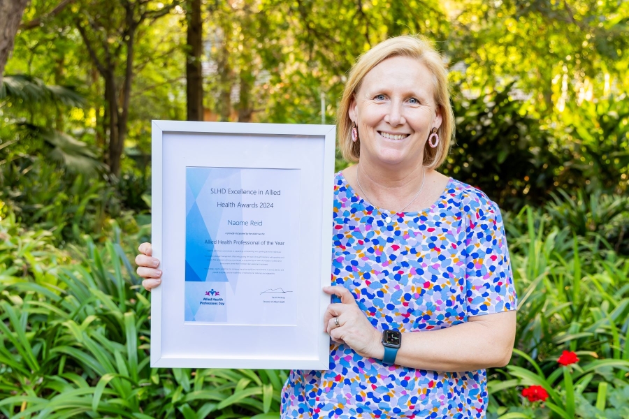 Woman standing outdoors holding a framed certificate