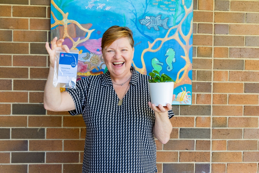 Woman holding a plant and award standing in front of a brick wall.